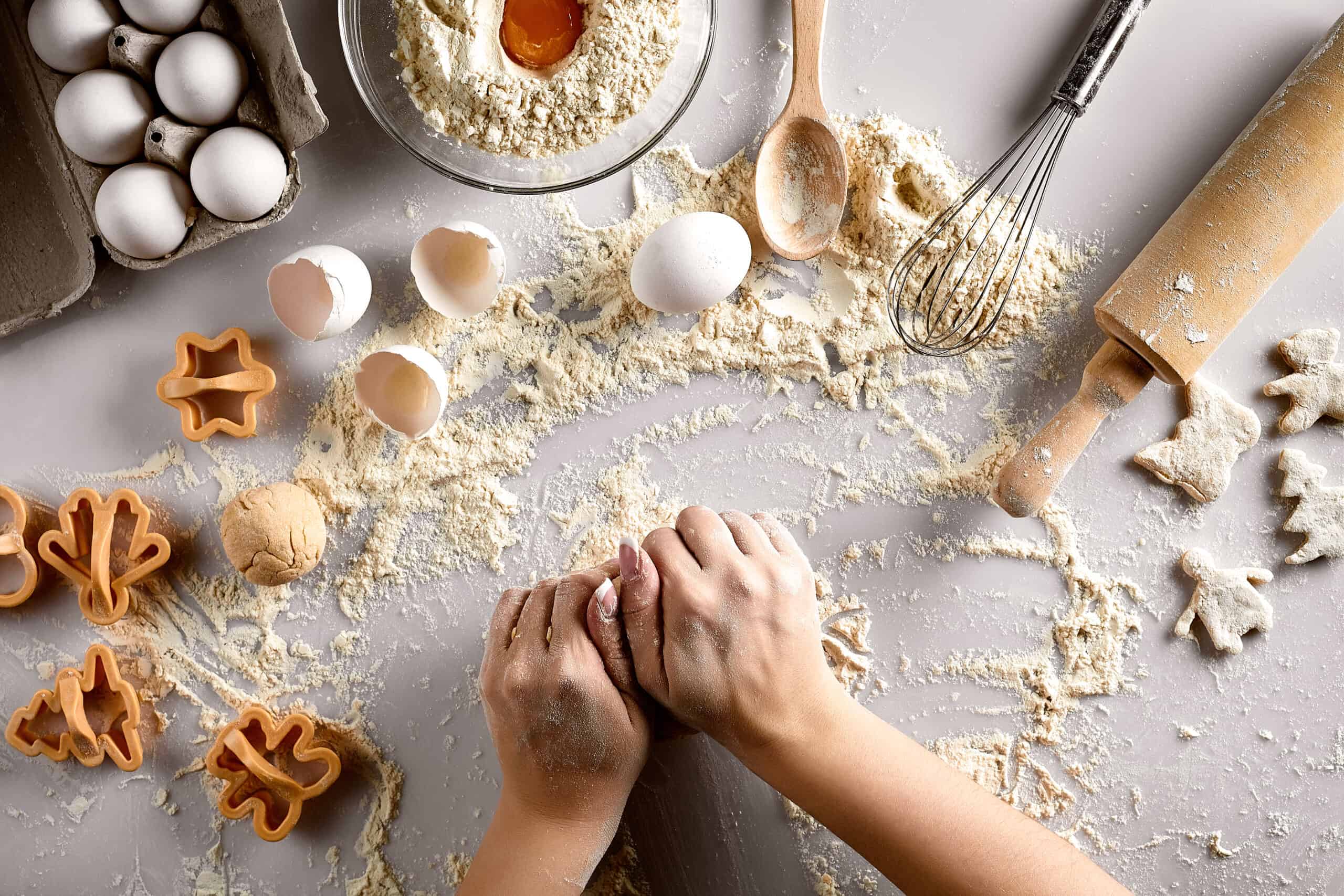 Baking supplies, raw dough and cookie cutters laid out on a white table